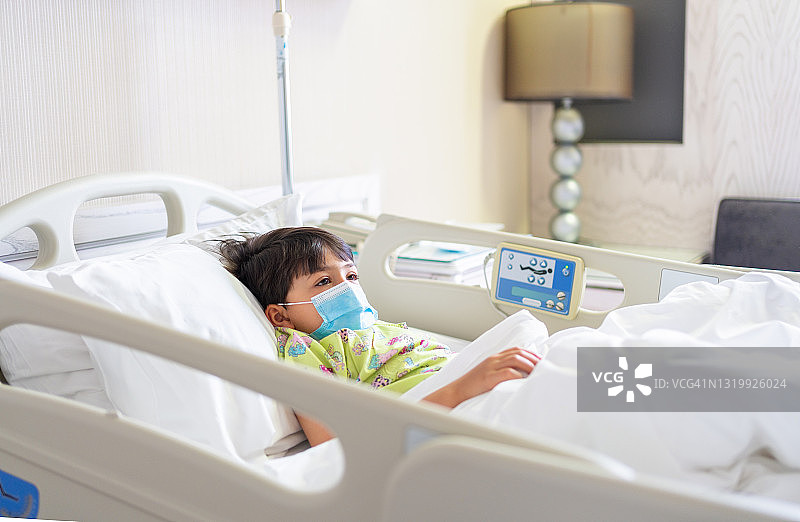 戴着防护口罩躺在医院病床上的小患者图片素材