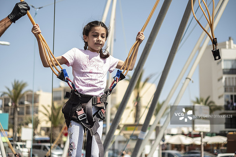 游乐园里准备玩蹦床的安全带小女孩图片素材