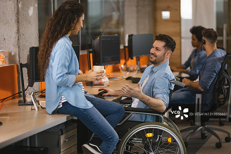 坐在轮椅上的程序员在办公室里与女同事聊天图片素材