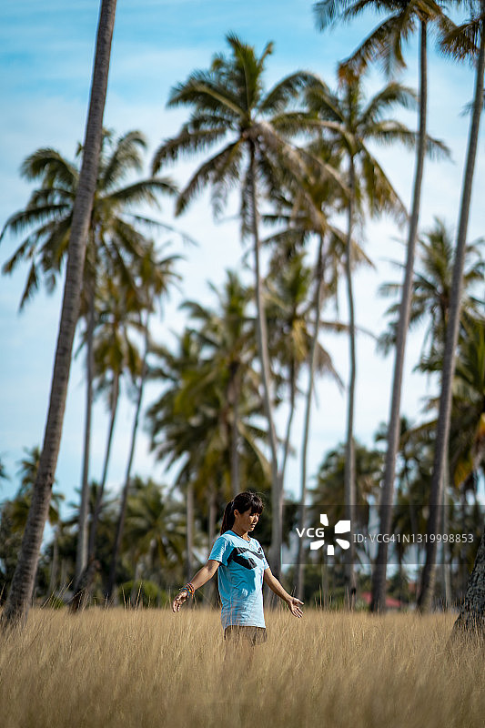 站在椰子树和黄色草地中的女孩图片素材