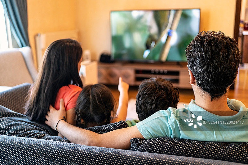 父母和两个孩子在家一起看电视图片素材