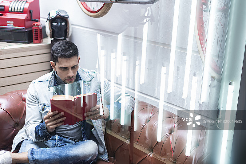 年轻的拉丁裔男子坐在他的店铺里，专心致志地读书图片素材