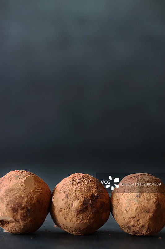 三个自制巧克力松露糖果，甘纳许中心，可可粉涂层，深灰色背景图片素材