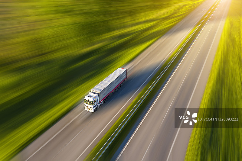 乡村绿色田野中卡车在沥青路上行驶的航拍景色图片素材