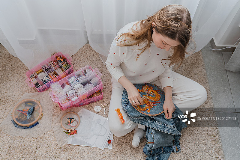 在家在地板上刺绣牛仔夹克的女人图片素材