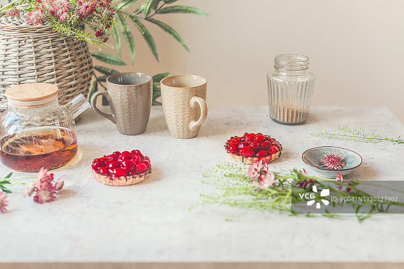 樱桃馅饼、茶杯、红茶玻璃茶壶、糖、鲜花和鲜花篮静物图片素材