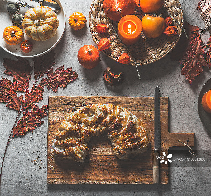 木制砧板上的自制辫子酵母面包，配有菜刀、秋叶和彩色南瓜图片素材