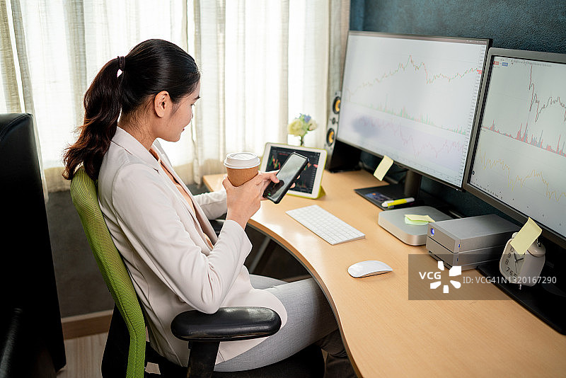 卧室里穿白色西装的亚洲股市投资者正在用电脑和平板查看股票图表图片素材