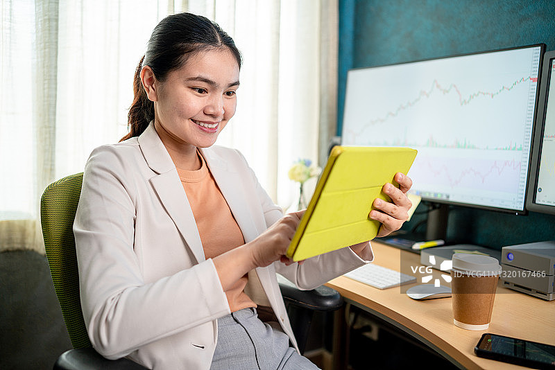 卧室里穿白色西装的亚洲股市投资者正在用电脑和平板查看股票图表图片素材