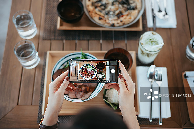年轻女性在餐厅用餐前用智能手机拍摄美味的烤牛肉饭套餐图片素材