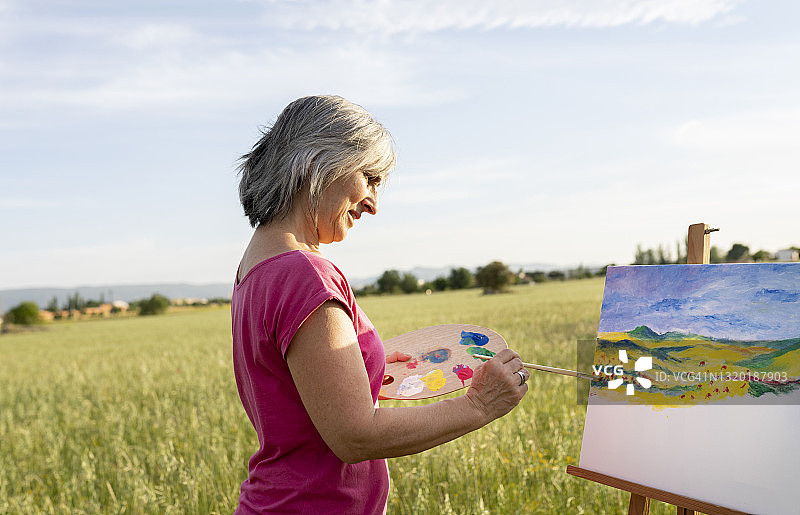 专注的老年妇女正在画乡村风景画图片素材