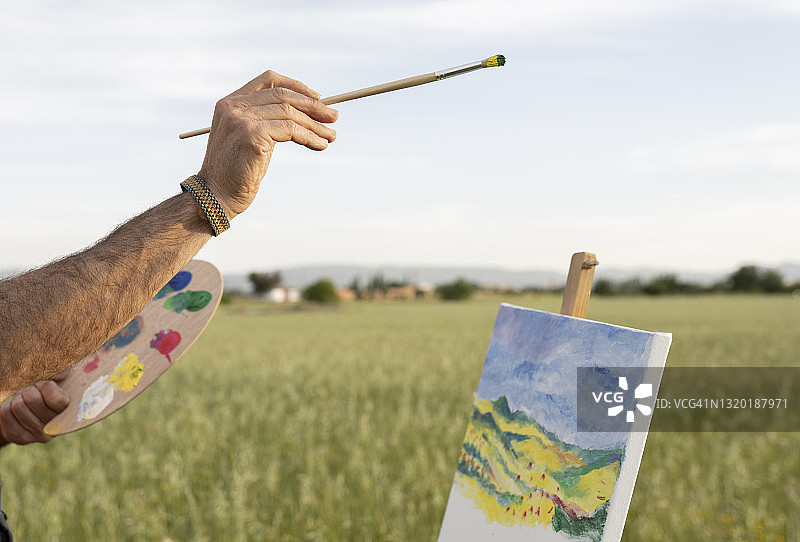 男人手握画笔和调色板在乡村画作前图片素材
