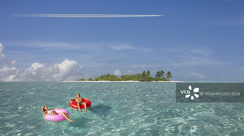 情侣躺在充气泳圈上，喷气式飞机划过白色条纹图片素材
