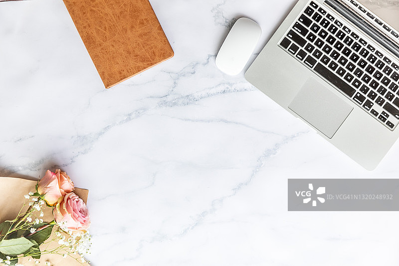 白色大理石背景上的笔记本电脑、笔记本和鲜花图片素材