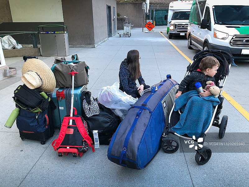 母亲和坐在婴儿车里的年幼男孩在机场堆放着大量行李图片素材