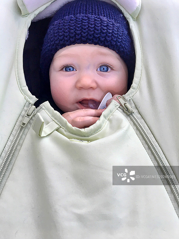 戴着蓝色羊毛帽，裹在汽车座椅和绿色罩子里的男婴图片素材