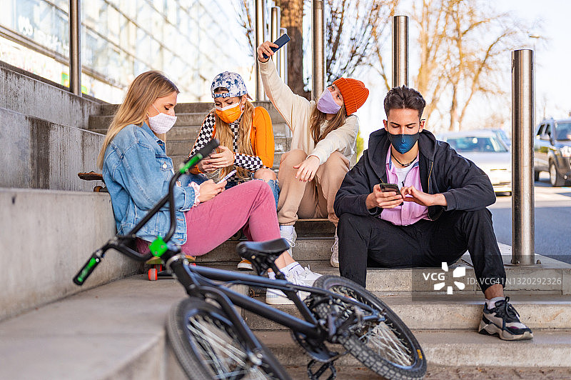 年轻的朋友们戴着口罩在户外玩滑板车和自行车图片素材