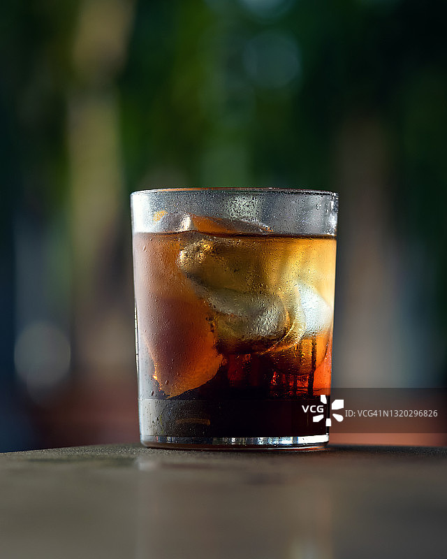 冰冻的玻璃杯，冰冻的酒精饮料或鸡尾酒。昏暗模糊的背景下，桌子上放着朗姆酒或威士忌加冰块。近距离拍摄。软的焦点。方形格式与复制空间的文本。侧视图图片素材