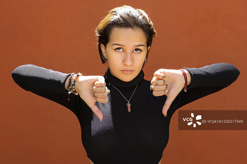 年轻的拉丁裔女人看着镜头，竖起大拇指向下图片素材