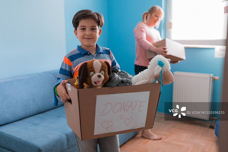 快乐的男孩抱着装满玩具的捐款箱。图片素材