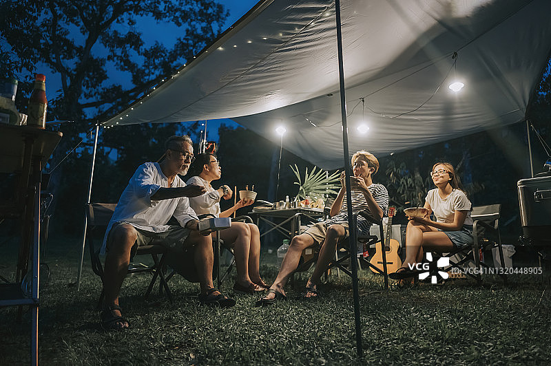 华人家庭与两个十几岁的孩子在露营帐篷里享用晚餐图片素材