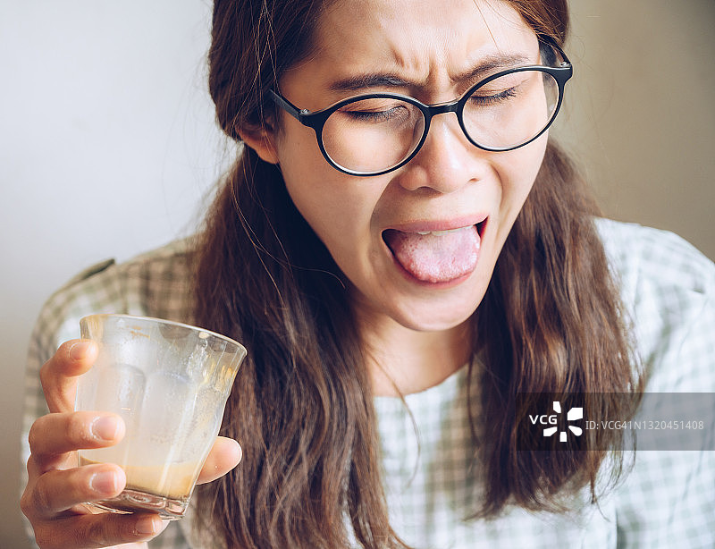 年轻亚洲女性在喝完浓咖啡后的面部表情图片素材