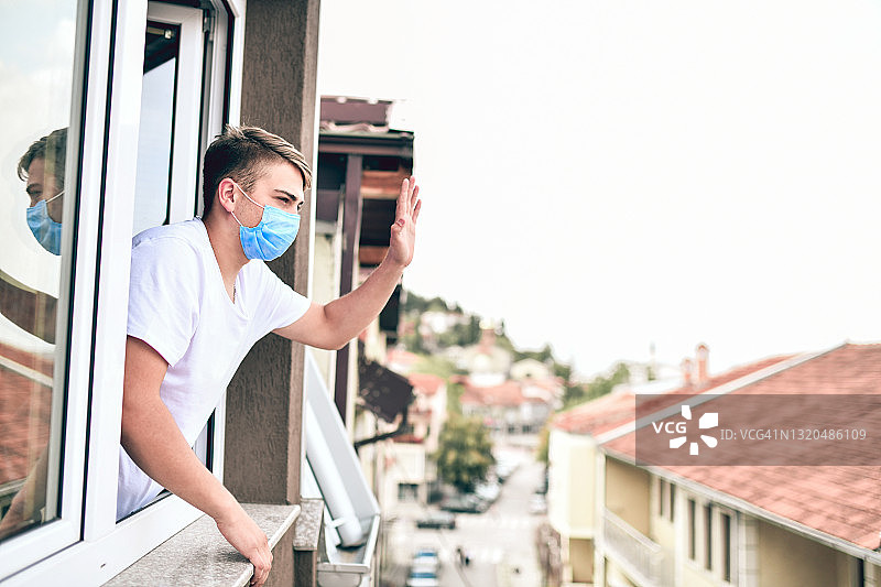 被隔离的COVID-19感染男子在窗户边向外面的朋友挥手图片素材