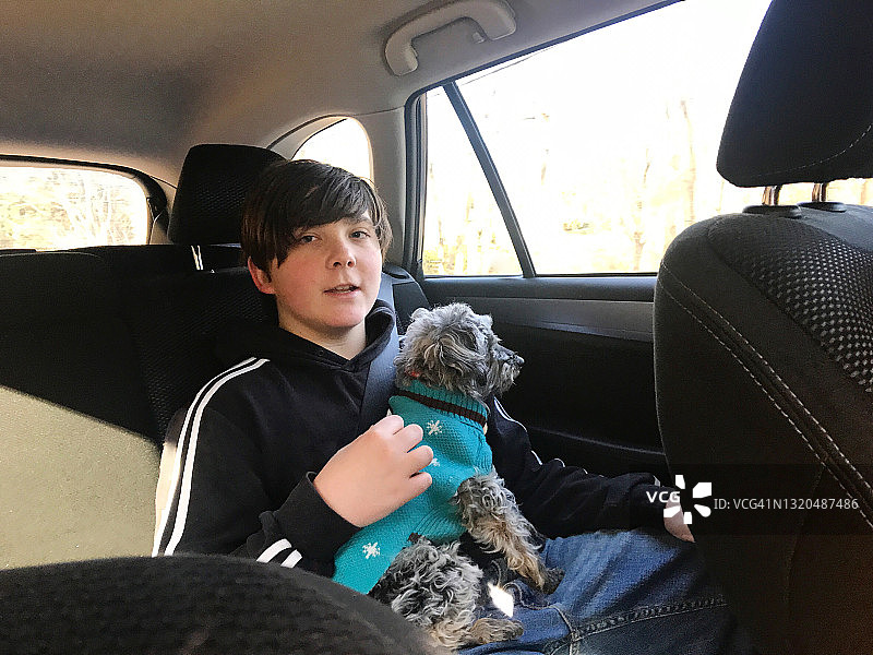 一个青春期前的男孩抱着一只小狗坐在车里图片素材