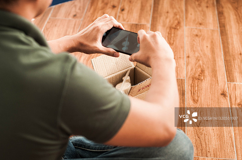 年轻东南亚男人室内用智能手机拍摄小纸箱图片素材