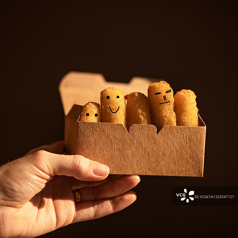 表情符号脸。男性手拿纸板容器装金块，上面画着简单的脸，黑色背景。家庭概念图片素材