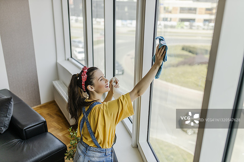 年轻漂亮的微笑女人用喷雾瓶和抹布清洁窗户图片素材