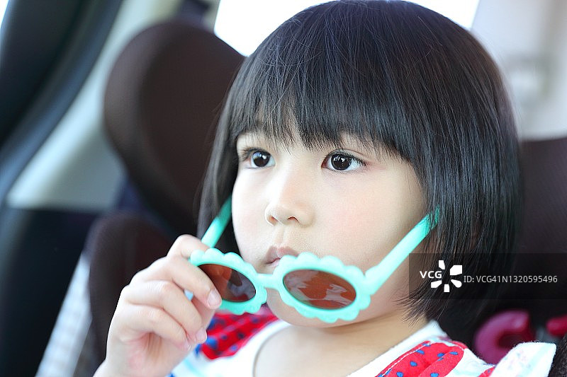 坐在汽车儿童座椅上戴着太阳镜的波波头小女孩图片素材