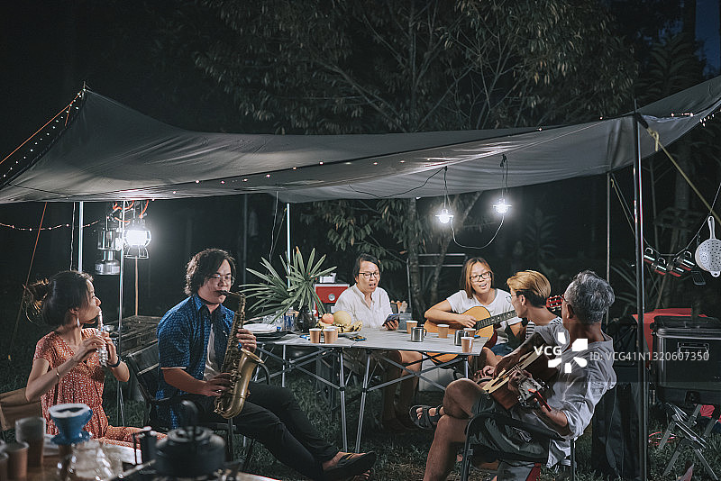中国家庭和朋友在花园派对上演奏乐器，夜晚在露营帐篷里欢聚图片素材