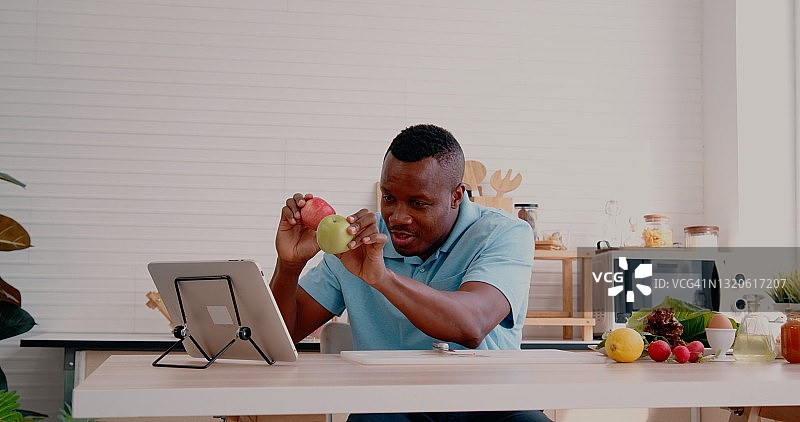 吃着苹果，用笔记本电脑保持社交距离，享受视频会议，观看网络研讨会，写笔记，家庭通话，与朋友打招呼，在家工作的非裔美国男人图片素材