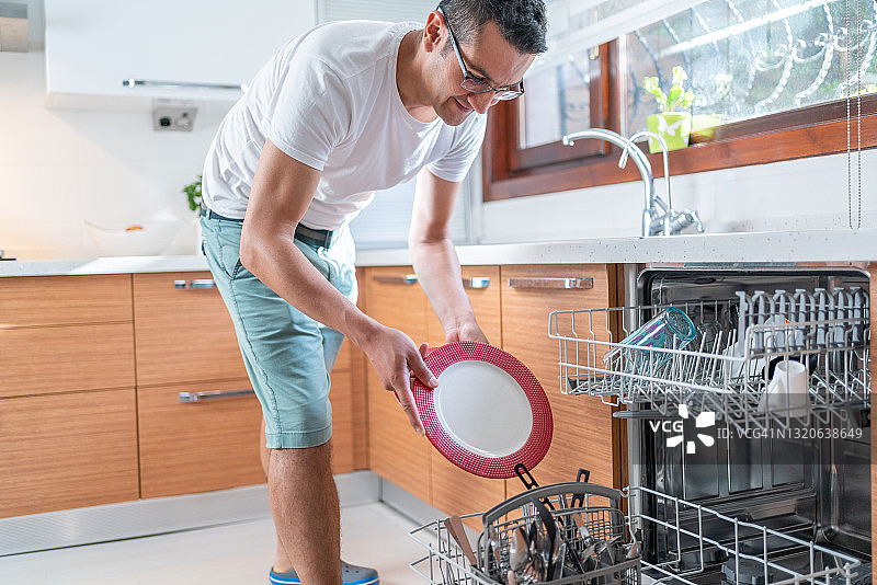 年轻男人将盘子放入厨房的洗碗机图片素材