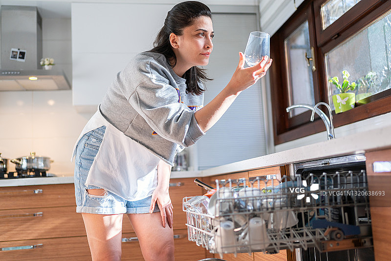 年轻女人从厨房的洗碗机里取出一个玻璃杯图片素材