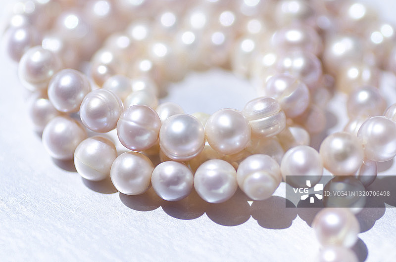 粉色珍珠项链缠绕在银色背景上的特写图片素材