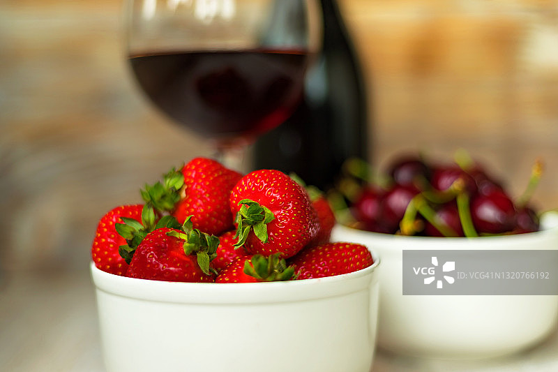 红酒瓶、酒杯、草莓和樱桃在木桌上的构图（模糊背景）图片素材