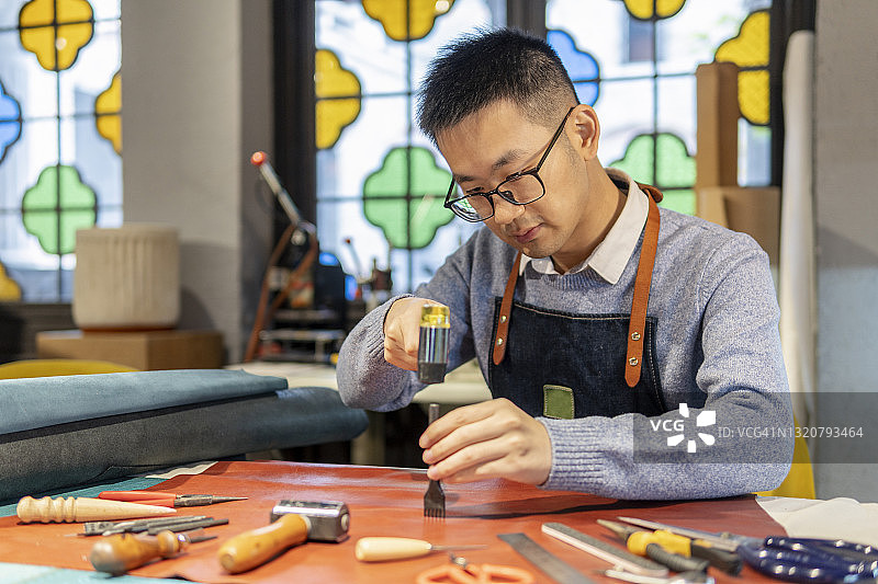 正在仔细制作皮革制品的亚洲皮革匠人图片素材