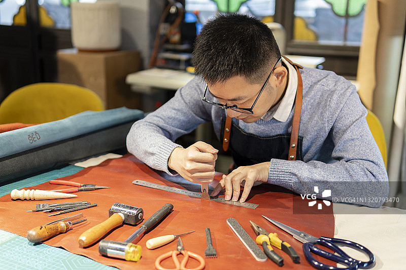 正在仔细制作皮革制品的亚洲皮革匠人图片素材