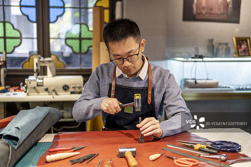 正在仔细制作皮革制品的亚洲皮革匠人图片素材