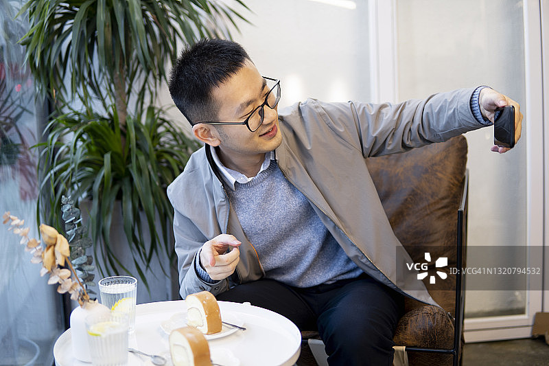 亚洲男人在咖啡馆吃瑞士卷并进行视频通话图片素材