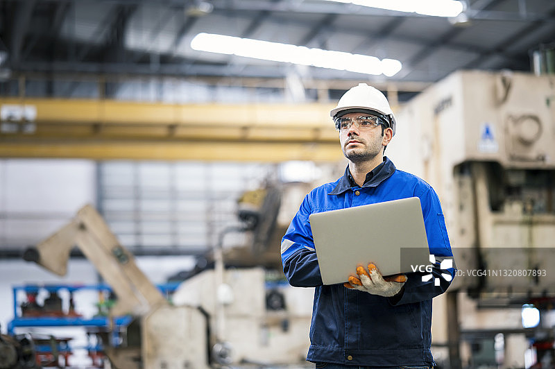 汽车工业中的汽车零件生产：生产线测量工程师使用大型液压冲压机并 holding laptop图片素材