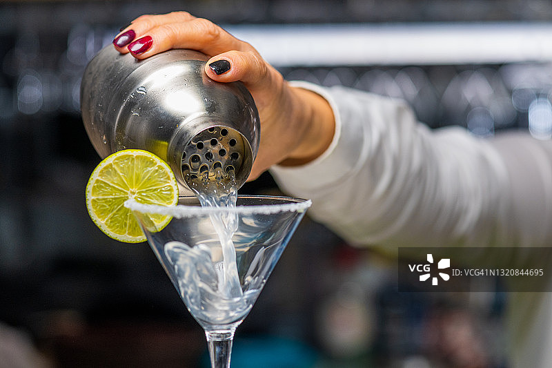 女调酒师用不锈钢调酒器将玛格丽特饮料倒入玻璃杯中图片素材
