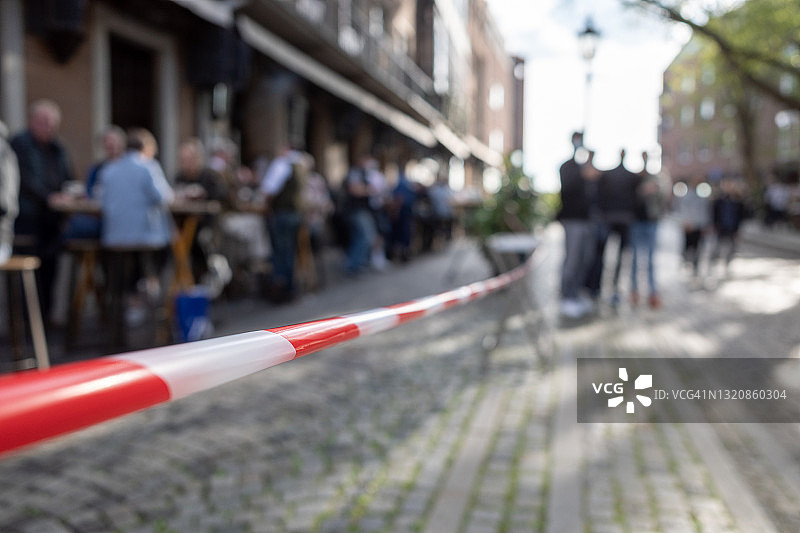 在封锁期间，德国杜塞尔多夫老城区红色和白色警戒线限制户外座位区的精选焦点视图。疫情期间人群享受重新开放的餐厅。图片素材
