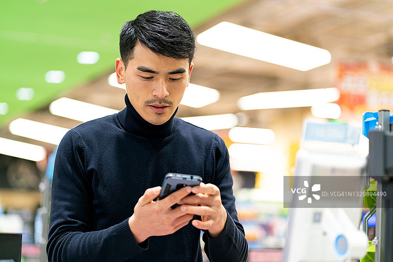 亚洲男顾客使用手机进行非接触式自助支付图片素材