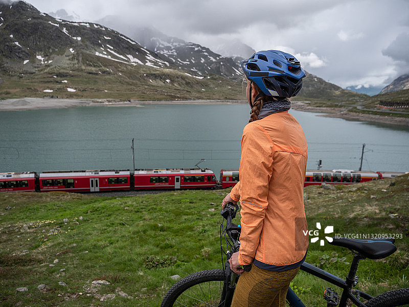 山地自行车骑行者在土路上看火车经过湖边图片素材