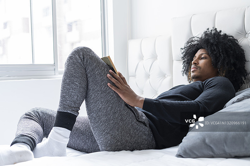 黑人男人穿着睡衣在床上看书图片素材