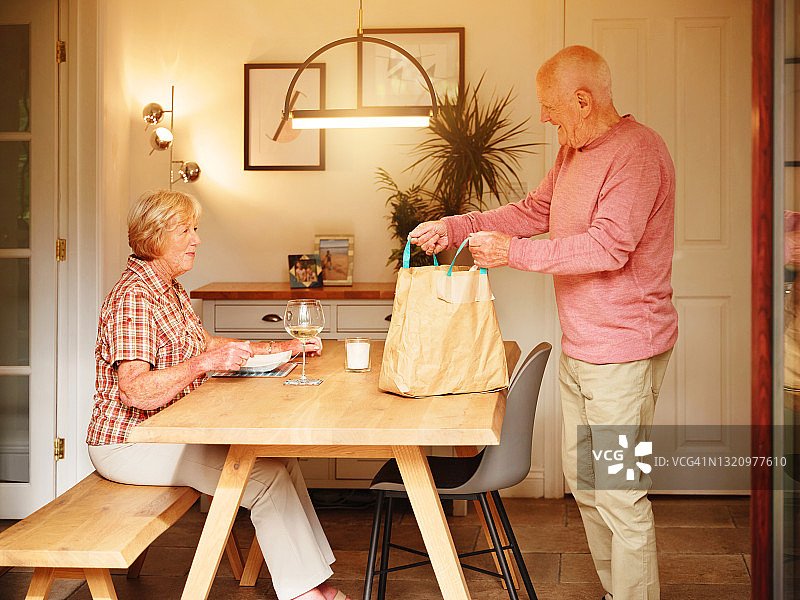 老年男子从纸袋中取出外卖食品与妻子在家享用图片素材