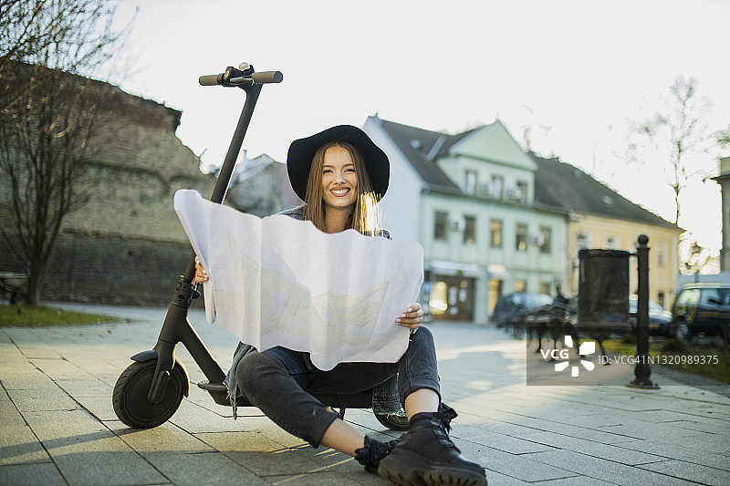 美丽的旅行者骑着电动滑板车查看地图以寻找方向图片素材